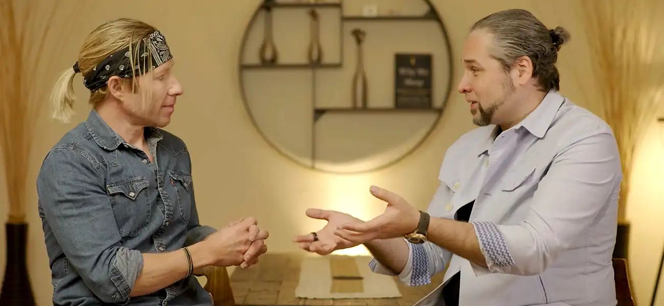 Two men sitting in a warm lit room talking to each other using hand gestures