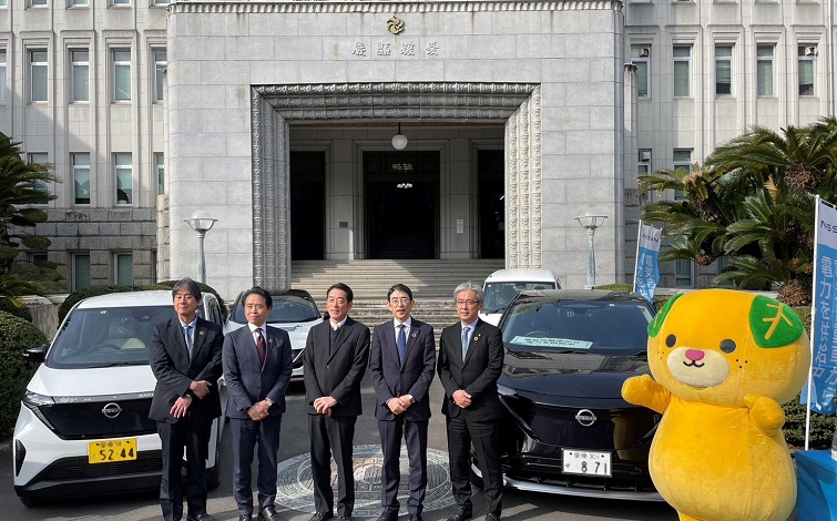 愛媛県庁のエントランス前、電気自動車の前で記念撮影する各代表者（男性5名）
