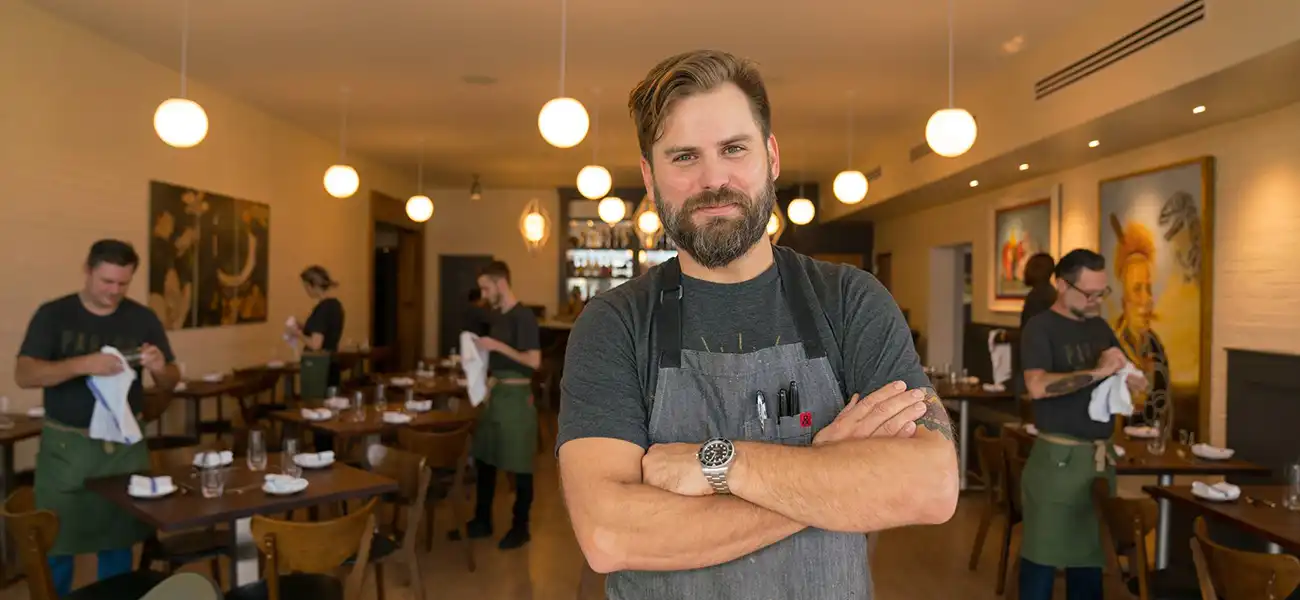 A man with a gray apron pausing in a resutaurant.