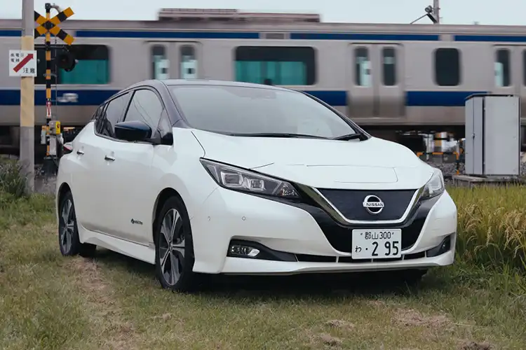 Un automóvil Nissan blanco estacionado frente a un tren en movimiento.