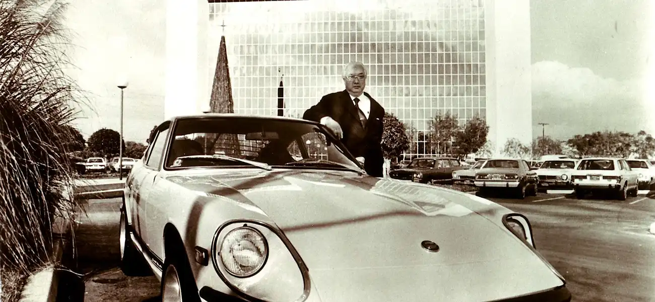 Yutaka Katayama standing next to Datsun Z in a black and white picture.