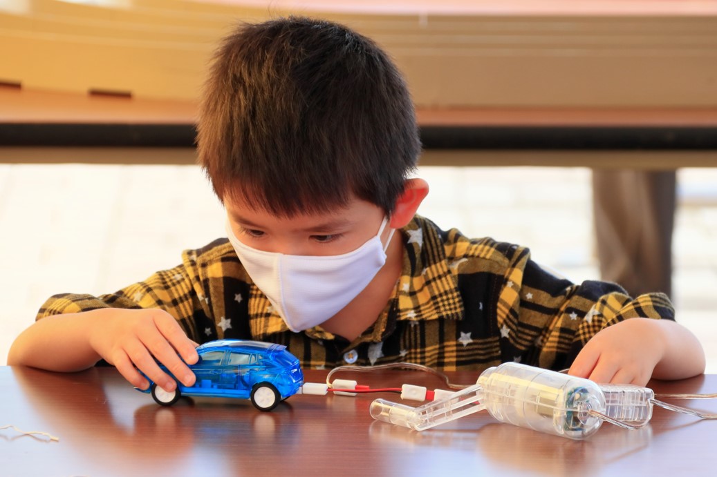 A boy wearing a mask and playing with a blue toy car.