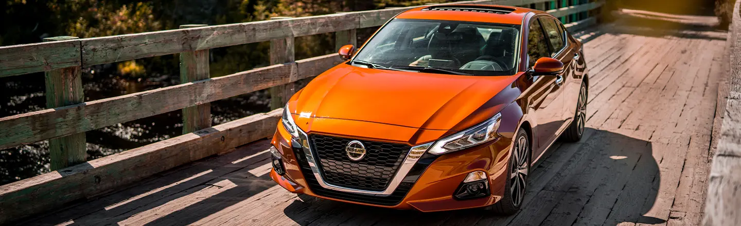 A 2020 Nissan Altima crosses a bridge surrounded by trees.