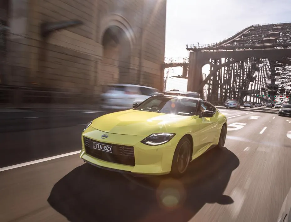A yellow Nissan Z driving in front of a bridge