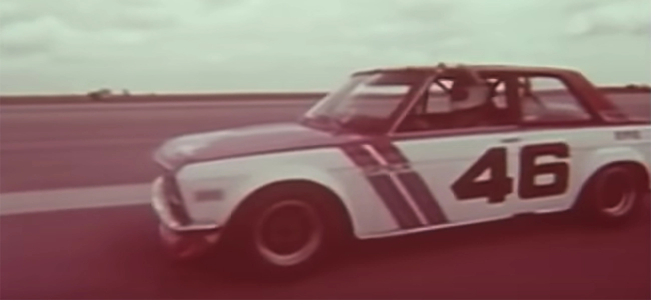 A black and white image of a Datsun driving on a road.