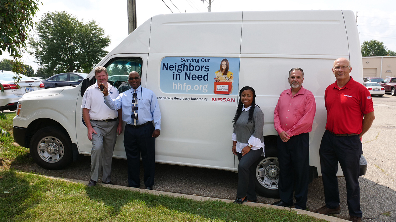 5 people pausing in front of a white van.