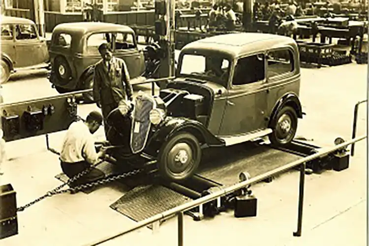 Una antigua fotografía en blanco y negro que muestra a dos personas trabajando en un automóvil.