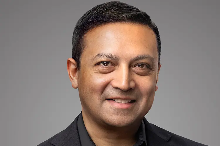 Ponz smiling from the chest up in a black suit and black button-up shirt against a gray background.