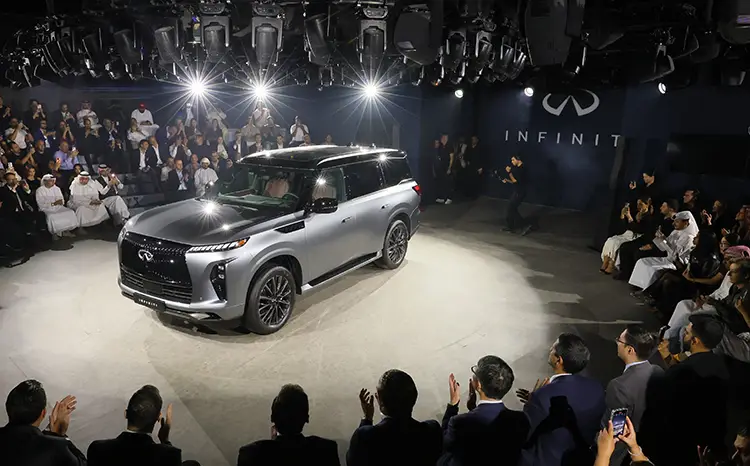 A gray INFINITI QX80 under lights at an event in Dubai with crowd watching and taking photos.