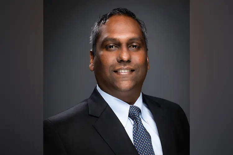 Aditya from the chest up, smiling, in a black suit, polka dot tie, and white dress shirt.