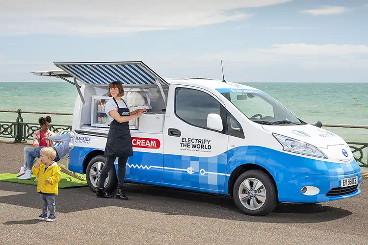 Una furgoneta de helados eléctrica blanca estacionada frente al océano.