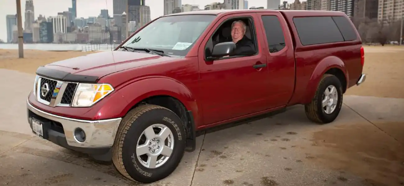 A red Frontier King Cab pickup parked in a park with Brian Murphy in the driver seat.