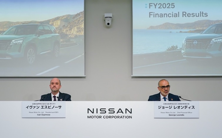 A press conference scene with two people seated side by side at the front of a conference room. Behind them, screens display images of vehicles and the text “FY2025 Financial Results,” with the “NISSAN MOTOR CORPORATION” logo shown on the central wall.