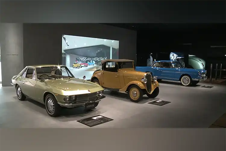 3 autos patrimoniales estacionados frente a una pantalla que dice "Nissan Heritage".