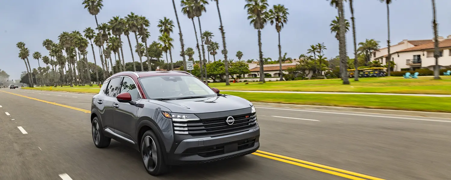 Front right 3/4 angle of a 2026 Nissan Kicks driving along a palm tree lined road.