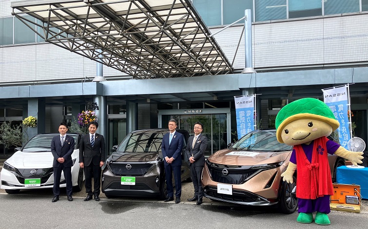 電気自動車の前で記念撮影する亀岡市、ニチコン、日産自動車の各代表者