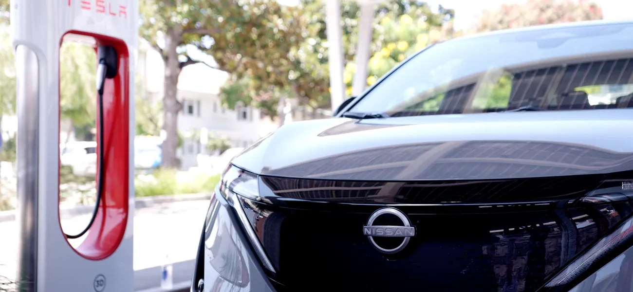 Close up of 3 /4 of a grey 2025 Nissan ARIYA in front of a Tesla charger