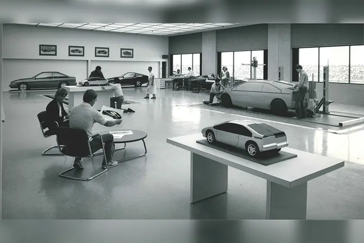 Black and white photo of serveral people in a room with model cars and images
