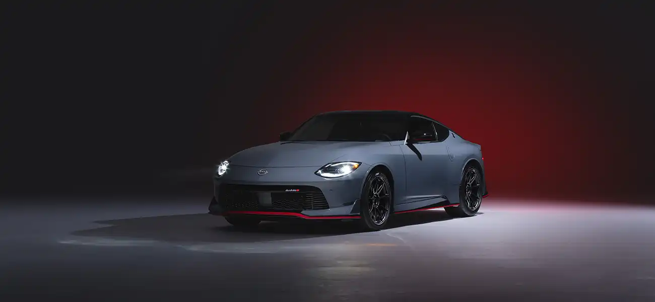 Front left 3/4 angle of a 2024 Z NISMO on a gray floor and dark red gradient background.