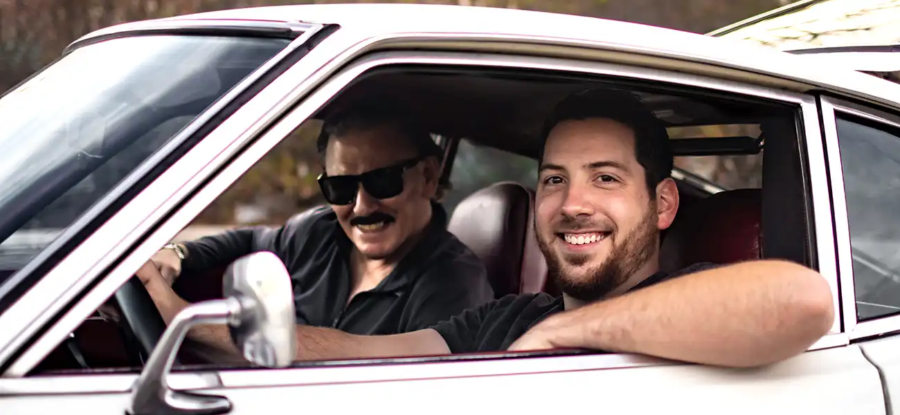 2 people sitting in the front seat of a white Nissan Z.