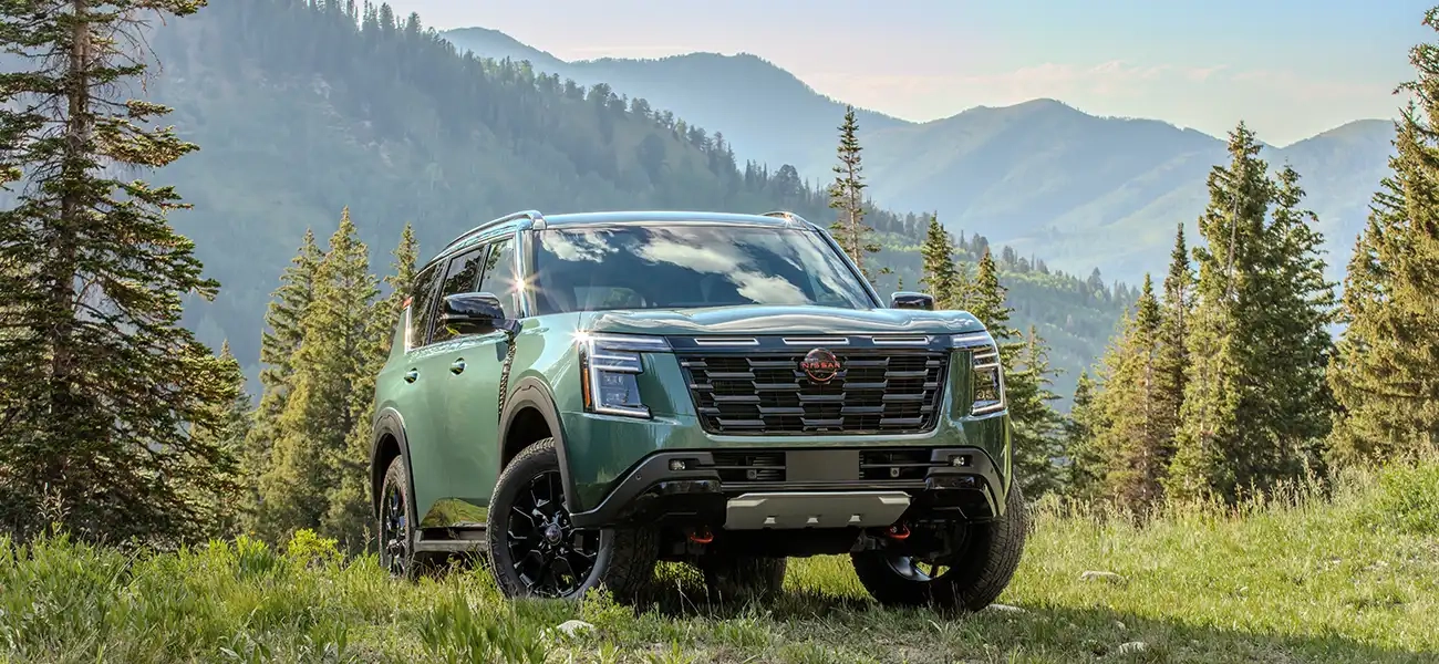 Tight front right 3/4 view of a 2025 Nissan Armada parked with its wheels turned on a grassy hilltop overlooking mountains.