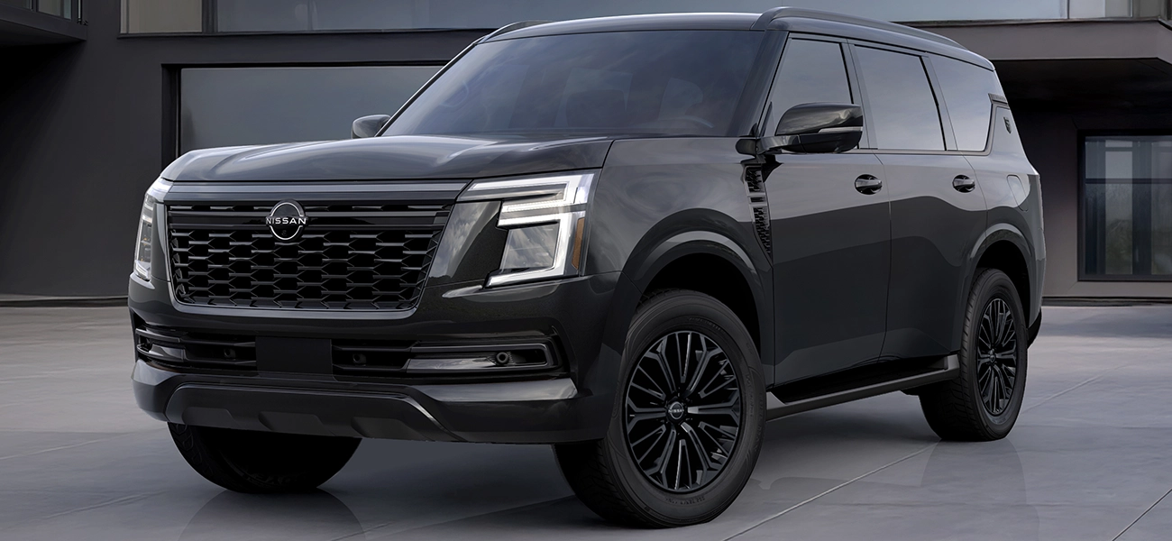 Front left 3/4 view of the 2027 Nissan Armada Dark Armor parked in front of a modern building.
