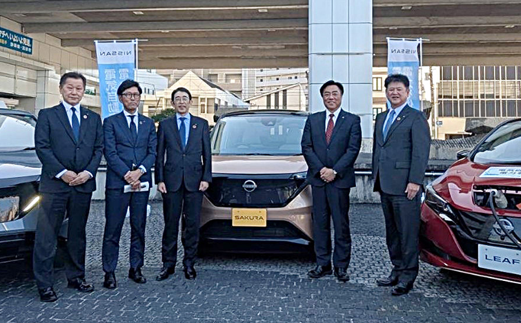電気自動車の前で記念撮影する各代表者