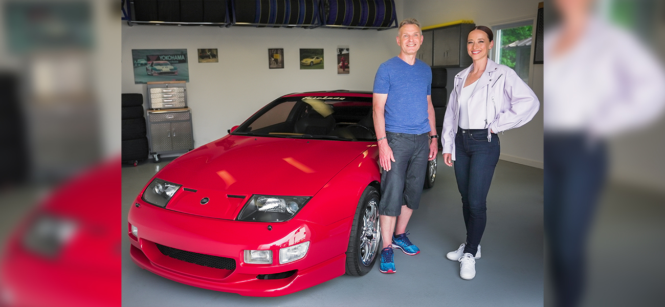 Two people standing next to red car and smiling