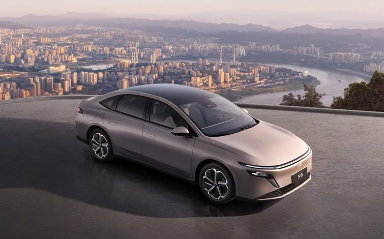 ベージュの日産「N6」が右斜め前向きに駐車されており、その背後には街並みが広がっています。