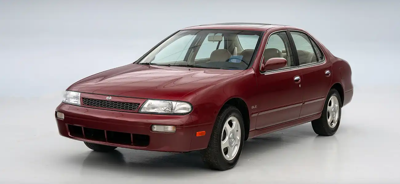 An image of a wine red 1993 Nissan Altima with a light background.
