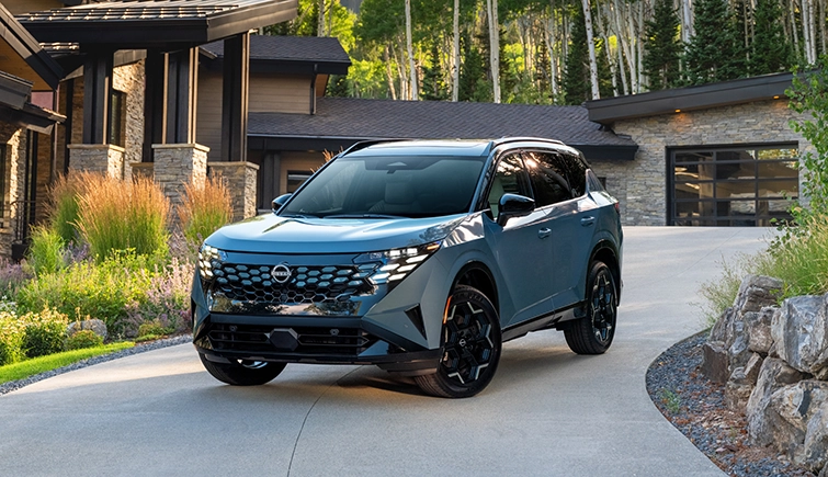 Front left 3/4 angle of the 2027 Nissan Rogue Hybrid Platinum parked in front of a house with trees behind.
