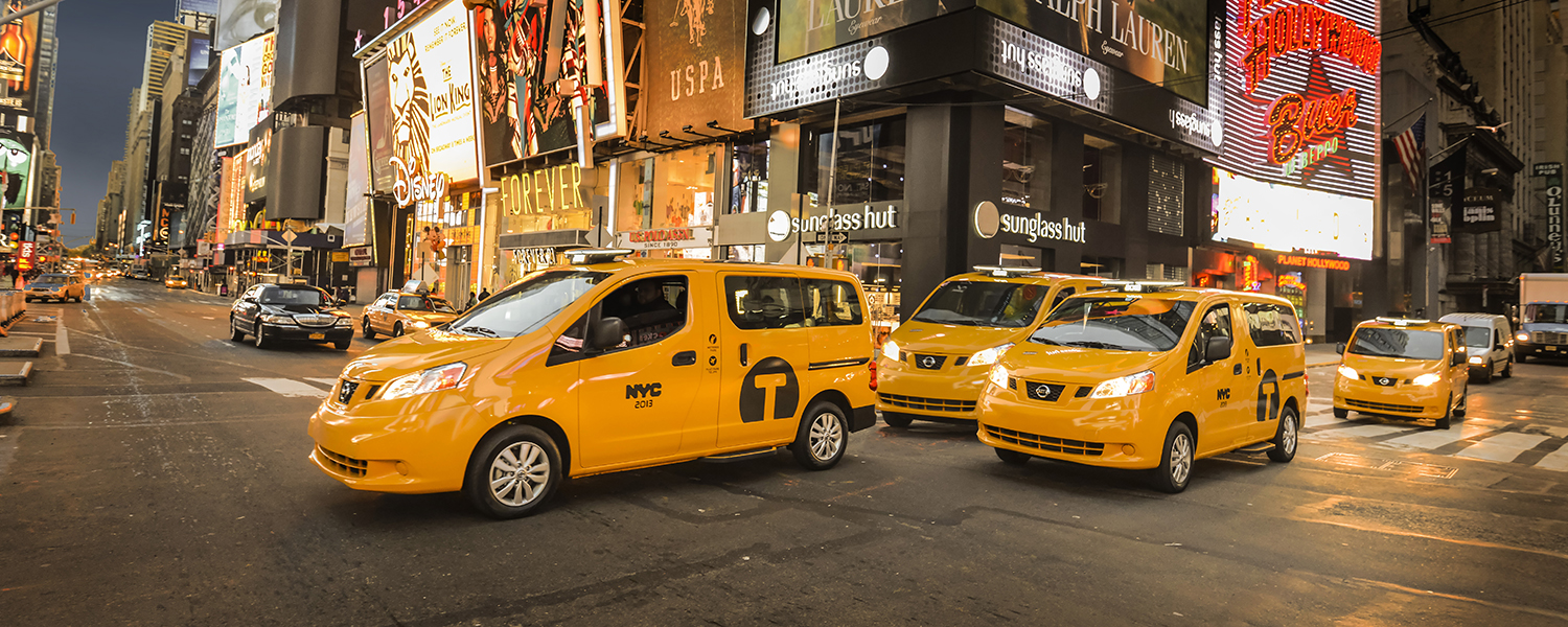 A group of 2014 Nissan NV200 Taxi driving on a busy street