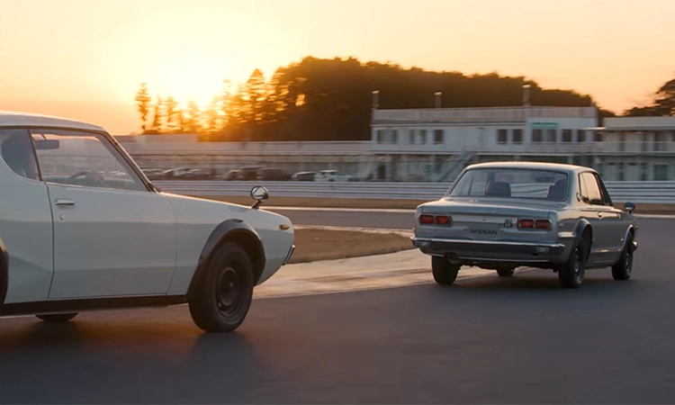 2 GT-Rs driving on a race track in sunset.