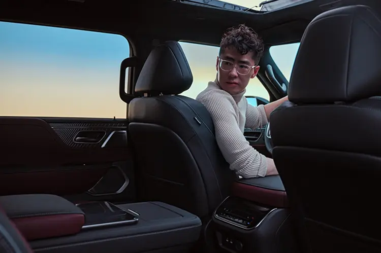 Tom hu in the front seat of a car twisted to look through the back window, the angle is from the rear passenger seat.