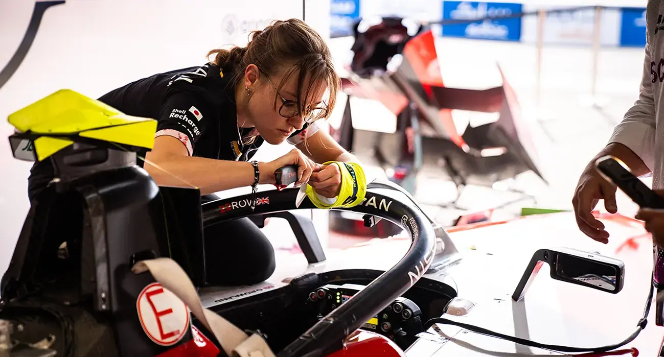 A woman in Nissan Formula E gear on a laptop near the race track.
