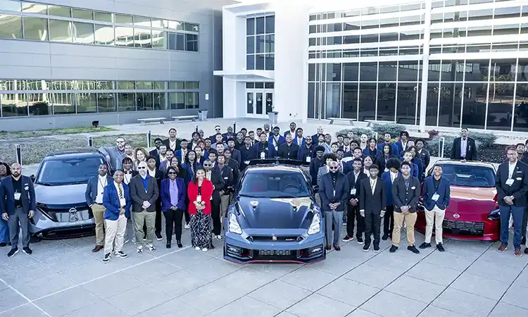 A large group of students, mentors and Nissan executives standing around a Nissan Ariya, GT-R and Z