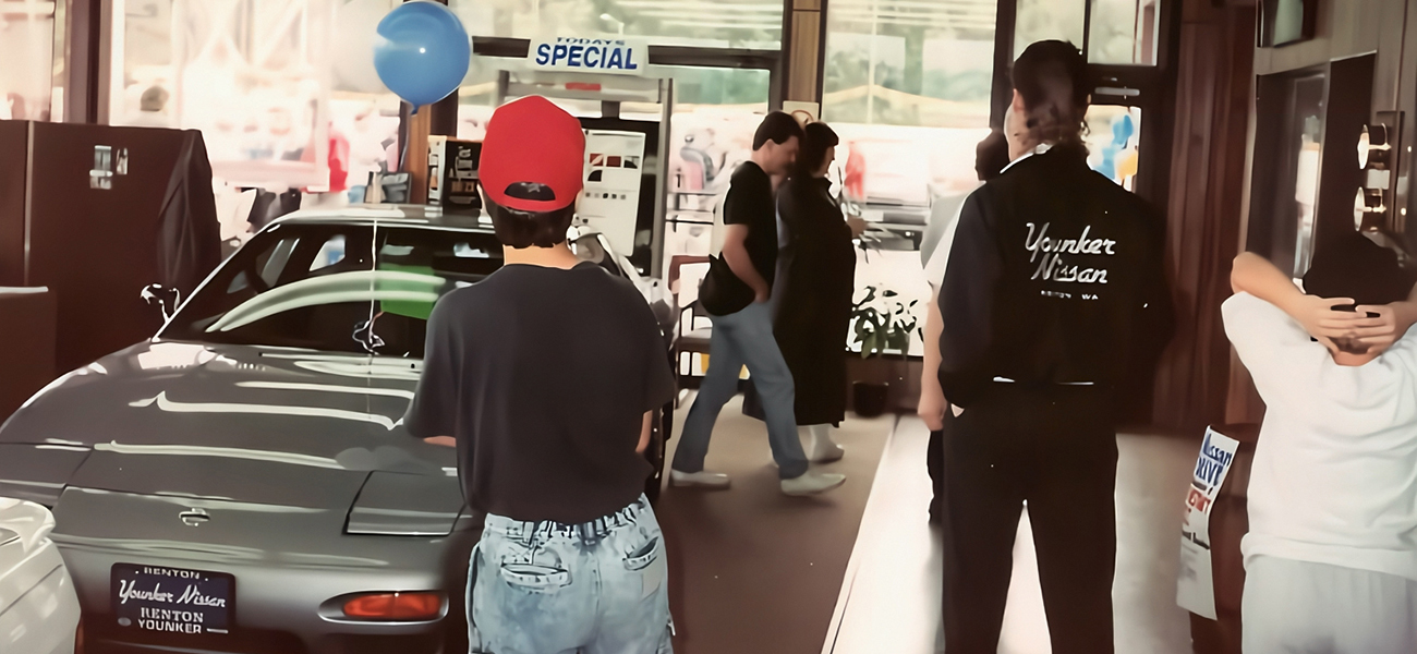 An image taken in 1980s, Younker Nissan with a few people looking at a car.