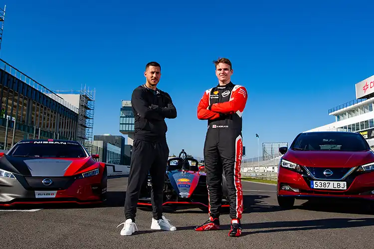 2 hombres posando delante de los coches Nissan en la pista de carreras.