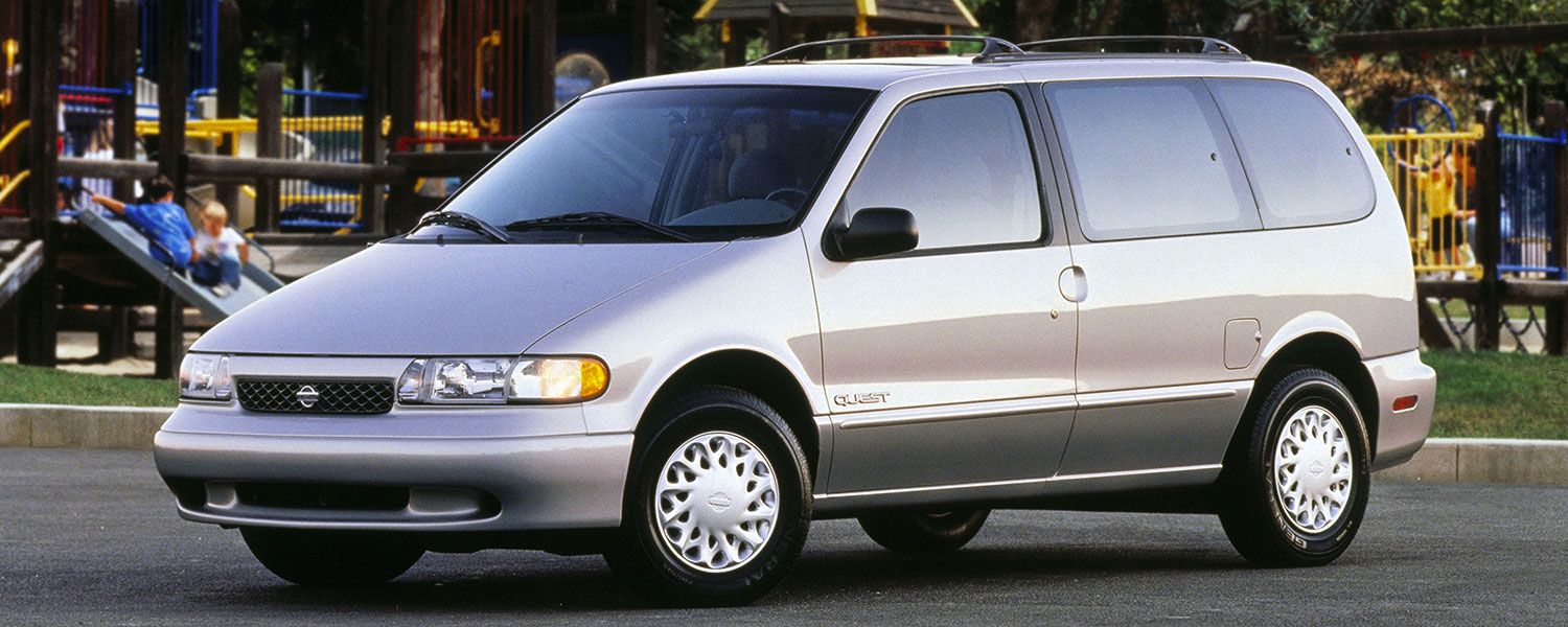 A silver Nissan Quest parked on a paved road in front of a children's playground.