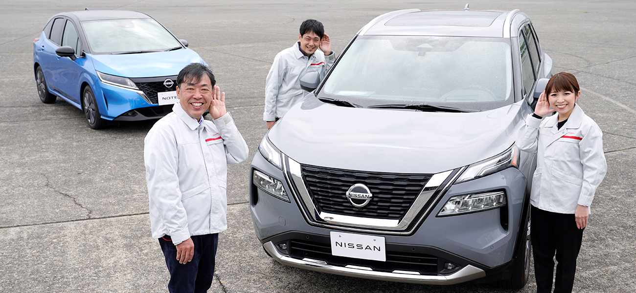 3 people surrounding a gray Nissan car.