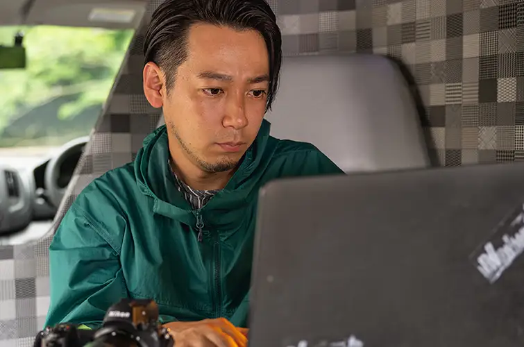 A man in a green shirt working on a laptop in the back of a car.