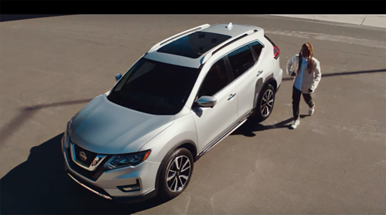 A person walking towards a silver Nissan Rogue in a parking lot.