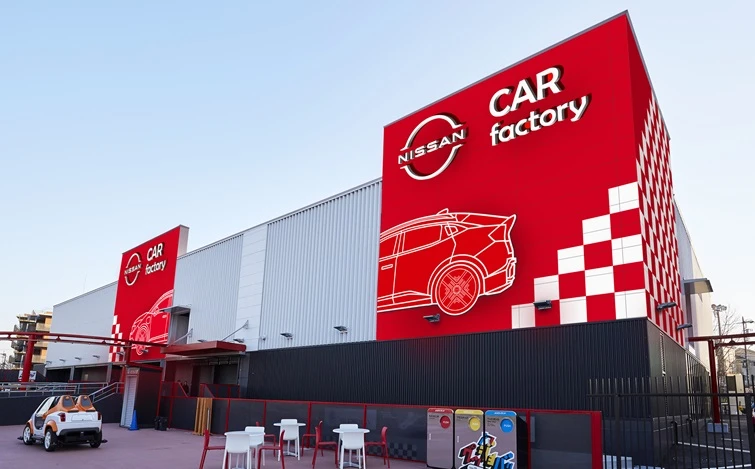 灰色の大きな建物に、赤い「CAR factory」の看板。看板には日産ロゴ、「日産リーフ」の線画、チェッカーフラッグ風の模様