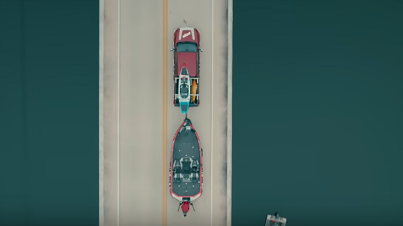 Nissan Titan with a boat attached to the back of the car driving on a bridge.