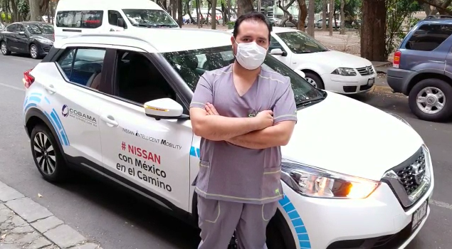 hombre con mascarilla bucal con brazos cruzados junto a un auto blanco