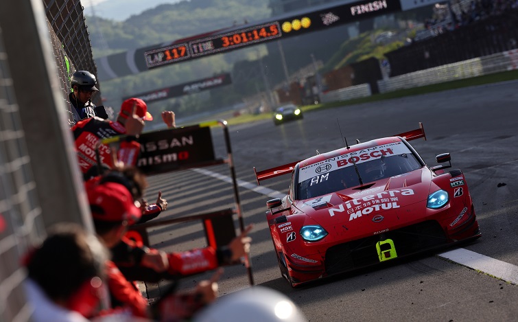 Red #3 Niterra MOTUL Z crossing the finish line with team crews waiting for the car at the pit wall