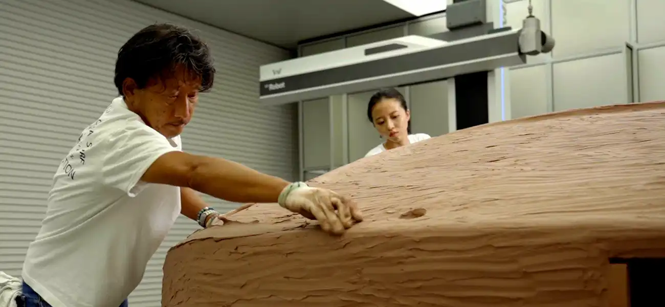 2 people working on a clay sculpture.