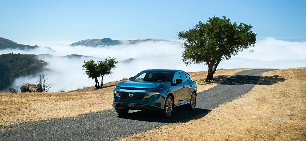 Vue avant gauche ¾ du Nissan Murano bleu garé sur une colline surplombant l'océan avec d'autres collines à côté.