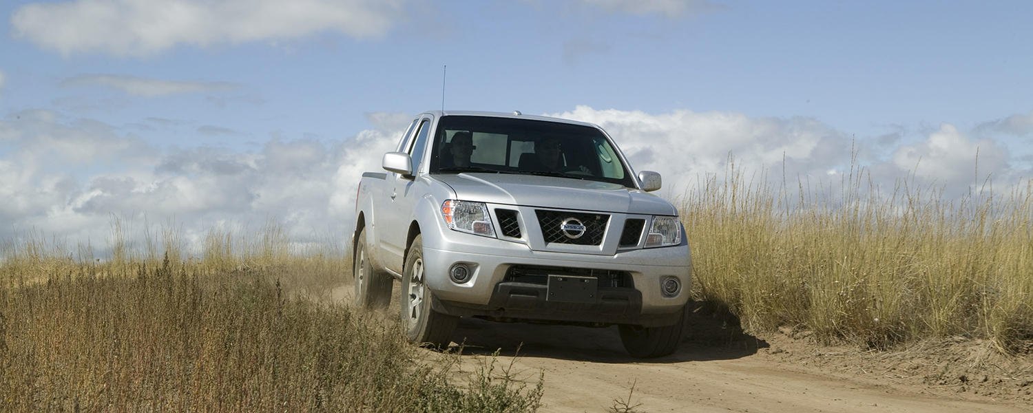 A silver Nissan Frontier driving on a sunny day through a dirt road.