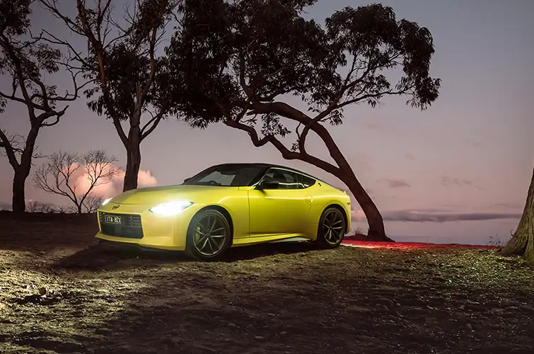 A yellow Nissan Z surrounded by 4 trees during sunset